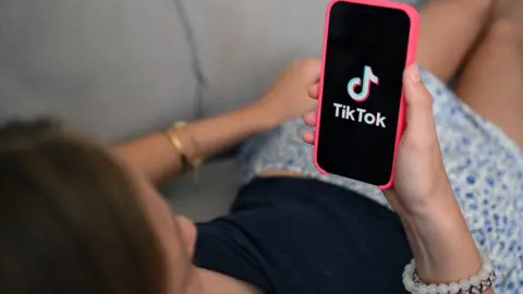 A teenager holds her phone displaying the TikTok logo