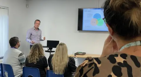 BBC The launch event - including people sitting at a desk