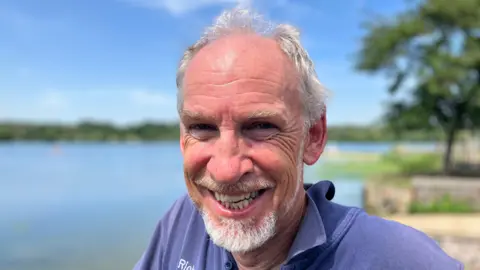 Shariqua Ahmed/BBC Richard, a man, with white hair and a small white beard, smiling for the camera.