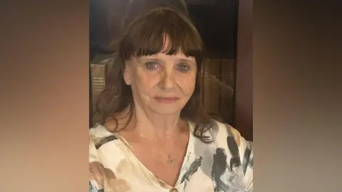 Caroline Hearn. She has brown hair with a fringe, wearing a cross chain and patterned v neck blouse.