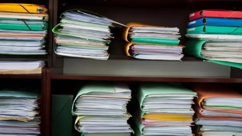 A file picture of large paper files stacked up in a bookcase.