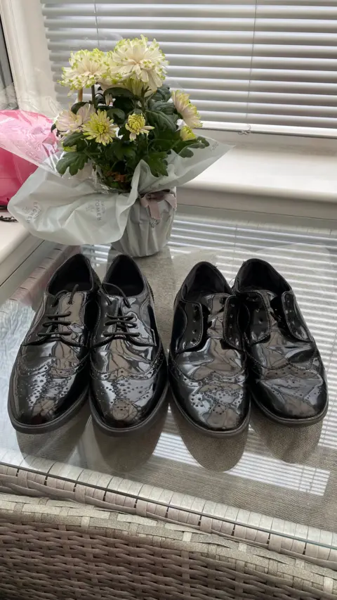 Two pairs of very similar patent leather girls' school shoes placed side by side on a table.