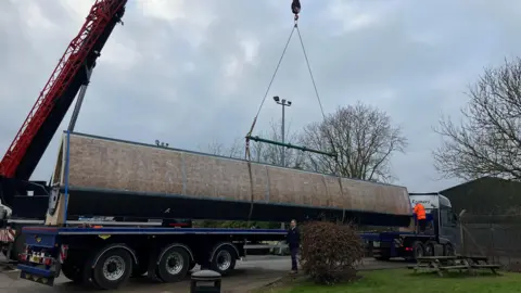 A huge blade dwarfing a man in high vis on the back of a lorry