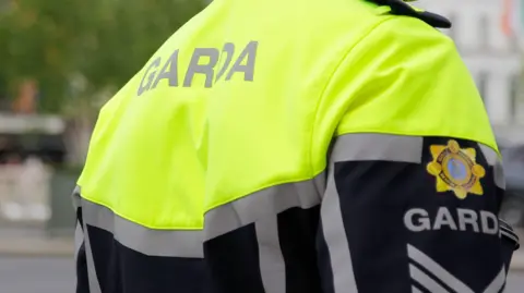 The back of a Garda Síochána (Irish police) uniform jacket. It is yellow hi-vis and black. 