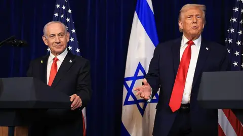 Getty Images A smiling Netanyahu, who has grey hair and wears a suit, at a lectern in during a press conference at Mar-a-Lago in December with Trump, who has blonde combed over hair and also wears a suit