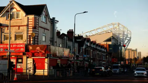 Reuters A Manchester United-themed off-licence can be seen in front of a row of terraced homes that open out alongside a road towards a stand of Old Trafford.