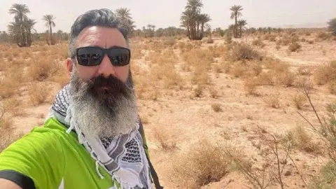 Barnardo's Mr Rigley in sunglasses and a bright green shirt in the Sahara