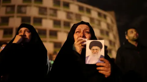 Reuters A woman holds on to a picture of Iran's Supreme Leader Ayatollah Ali Khamenei at the Vali-Asr Square, after he was killed in Israeli and U.S. strikes on Saturday,