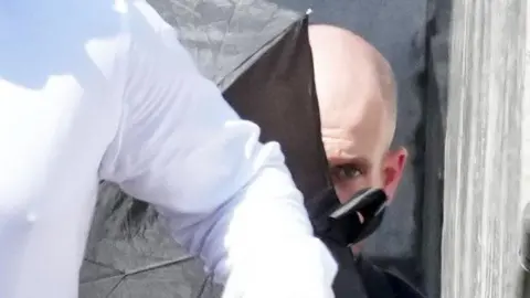 A close-up image of Jake Mullarkey outside court, partially hidden behind a black umbrella.