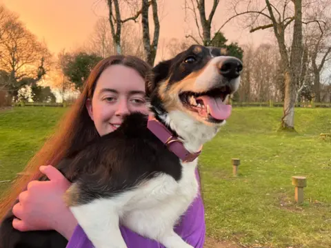 Jessica, with long brown hair, cuddles Zola, a black and white collie. Zola 