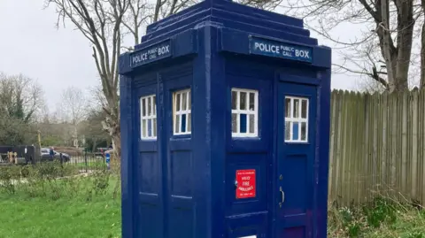 A blue structure with the words police public call box at the top. There are two sets of windows on the two visible sides.