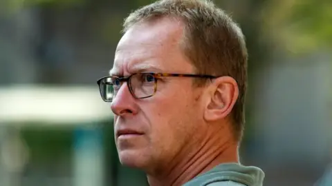 Mark Johnson looks sterm in glasses and a green shirt