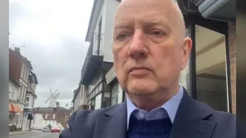 Local Democracy Reporting Service The chairman of the Environment and Transport Cabinet Committee at Kent County Council, Cllr Sean Holden, pictured in a navy suit jacket, a royal blue jumper and a pale blue shirt underneath.