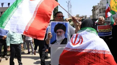 man waves Iranian flags and holds pic of Iran's supreme leader Ali Khamenei