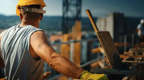 A closeup picture of a construction worker on top of a building in the sunshine, taking a short break.