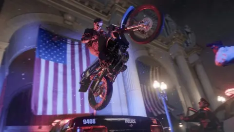 Activision A screenshot from a video game shows a man on a motorcycle jumping in the air over a police car in front of a building with an American flag