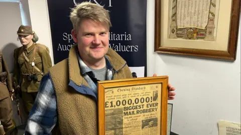 BBC Vince Scopes from C & T Auctioneers holds a framed front page of The Evening Standard from 1963 with the headline '£1,000,000 BIGGEST EVER MAIL ROBBERY'