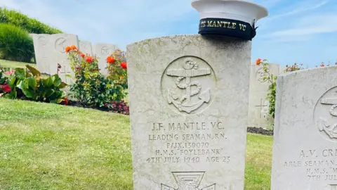 Portland Port Wreaths and a Royal Navy cap at the grave of Leading Seaman Jack Mantle VC at the Royal Naval Cemetery on Portland. It's a sunny day.