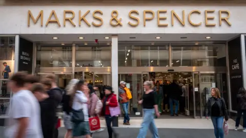 A M&S storefront with the words 'Marks & Spencer' above the doors to the store and shoppers walking outside the store, pictured in Bath in September 2024