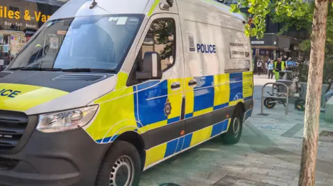 A police van parked on a town centre street during the daytime.