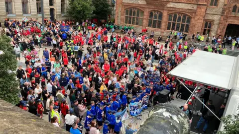 A crowd of young footballers in team colours gather in Derry's Guildhall Square