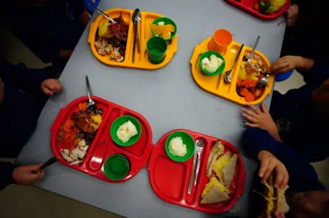 Two yellow and two red trays of school meals on a grey table, seen from above.