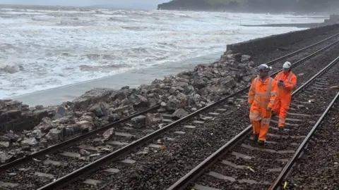 Railway workers are seen inspecting a crumbled sea wall at Dawlish.