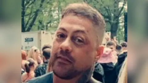 Facebook A headshot of a man with a neck tattoo. He is looking directly into the camera and there is a crowd of people in the background. 