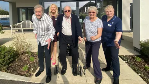Care home residents (left to right front row) Phil Edwards, Leonard Symonds and Ann Moore, from Heathland House are posing in front of the building to show they are set to Race Across Dorset. Deputy manager Sarah Gibson Clarke is beside them. Deborah Holmes is in the back row.