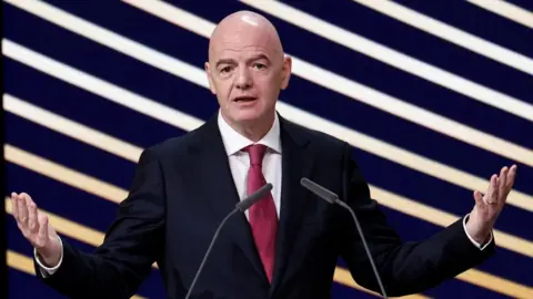 FIFA president Gianni Infantino speaks during an event, standing in front of a purple and yellow striped background.