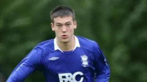 Jack Rutter in his younger years, running along a pitch in a long sleeved, blue football jersey with white writing and a white collar