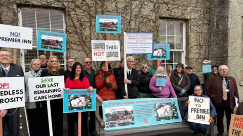 A picture of protesters holding up different signs outside the front of a building. 