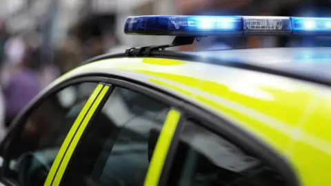 A police car with the blue lights on attending a crime scene (stock photo)