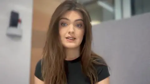 Kat Cereda has long brown hair. She is wearing a black T-shirt.