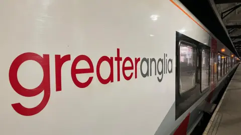 Side view of a Greater Anglia train with carriages running the length of the platform at a station