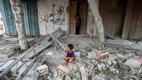 Reuters A Palestinian boy sits at the site of an Israeli strike on a house in Maghazi refugee camp, in the central Gaza Strip (14 August 2024)