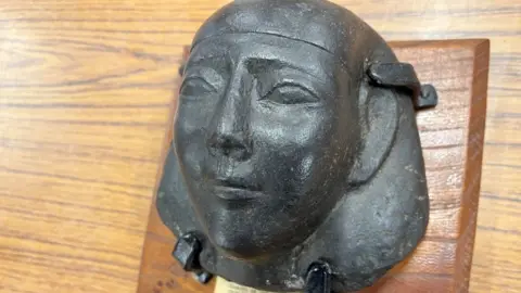 A black stone head, mounted on a substantial wooden board
