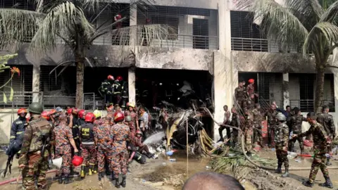 Reuters Firefighters and soldiers work next to the wreckage of an air force training aircraft after it crashed into Milestone College campus, in Dhaka, Bangladesh, 21 July 2005