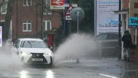 PA Media A vehicle is driven through floodwater after heavy rain in Warwick, more than 200 flood alerts are in place in the UK as Storm Bert continues to sweep across the country.