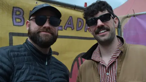 Valtos' Daniel Docherty and Martyn MacDonald standing in front of a yellow Belladrum banner in the press area at Belladrum.