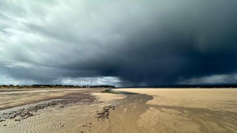 A dark raincloud hangs over a wide beach in Nairn, Highland