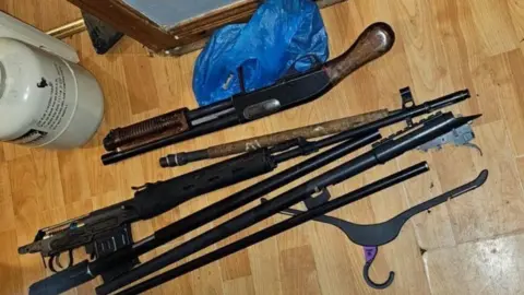 A number of firearms lying on a wooden floor