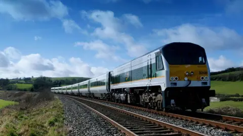 An Enterprise train on a track. It is yellow and green. 