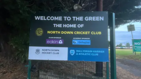 A large green sign outside the entrance to North Down Cricket Club.  It reads: "Welcome to the Green, the home of North Down Cricket Club.'"