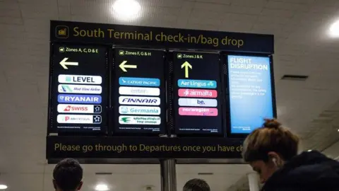 JackTaylor/GettyImages People look at the check in/bag drop sign at South Terminal at Gatwick Airport, West Sussex