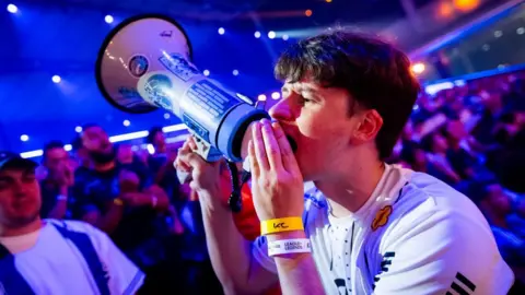 Esports Foundation A fan at the Esports World Cup shouts into a megaphone, attempting to drum up support for his team.