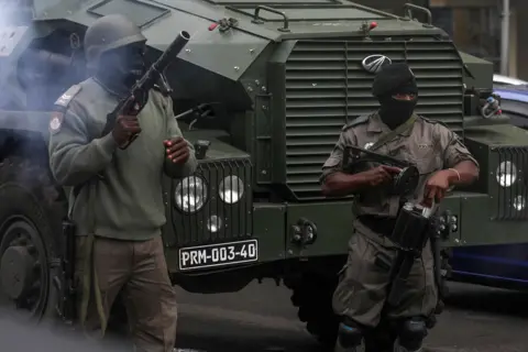 Reuters Two masked Mozambican police officers try to disperse people gathered to participate in a rally called by presidential candidate Venâncio Mondlane over the killing of two of his supporters, in Maputo, Mozambique - Thursday Hai, October 21, 2024