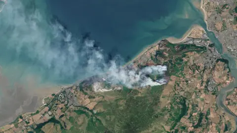 Aerial image of land with white smoke billowing from it.