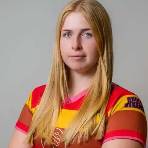 Bicester RUFC Jennie Logan looing at the camera with her long blonde hair over her shoulders. She is waring a bright, stiped T-shirt.