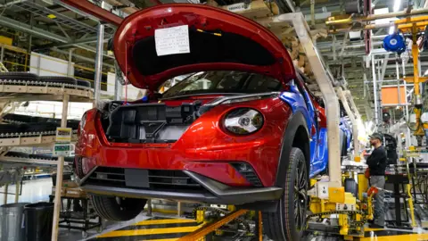 Reuters A car being built at Nissan's Sunderland factory. It is in the air on a conveyor with another car behind it.